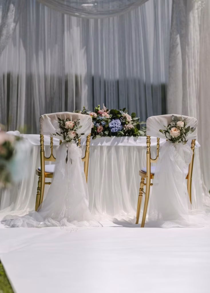 Goldene Brautpaarstühle mit Rosen und Blumendekoration stehen am Hochzeitstisch. blumenkultur - Eventfloristik Wien