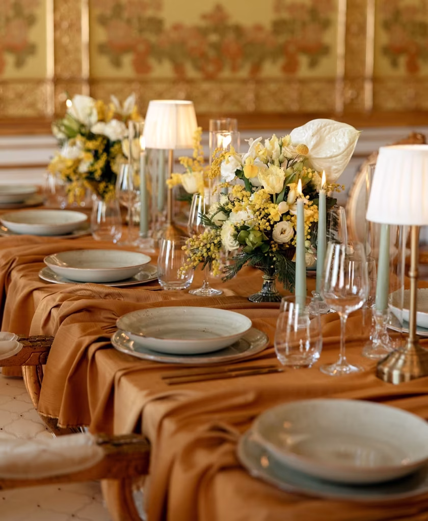 Elegante Tischdekoration mit gelb-weißen Blumen und goldenen Kerzenständern in einem historischen Saal. Hochzeitsfloristik - blumenkultur
