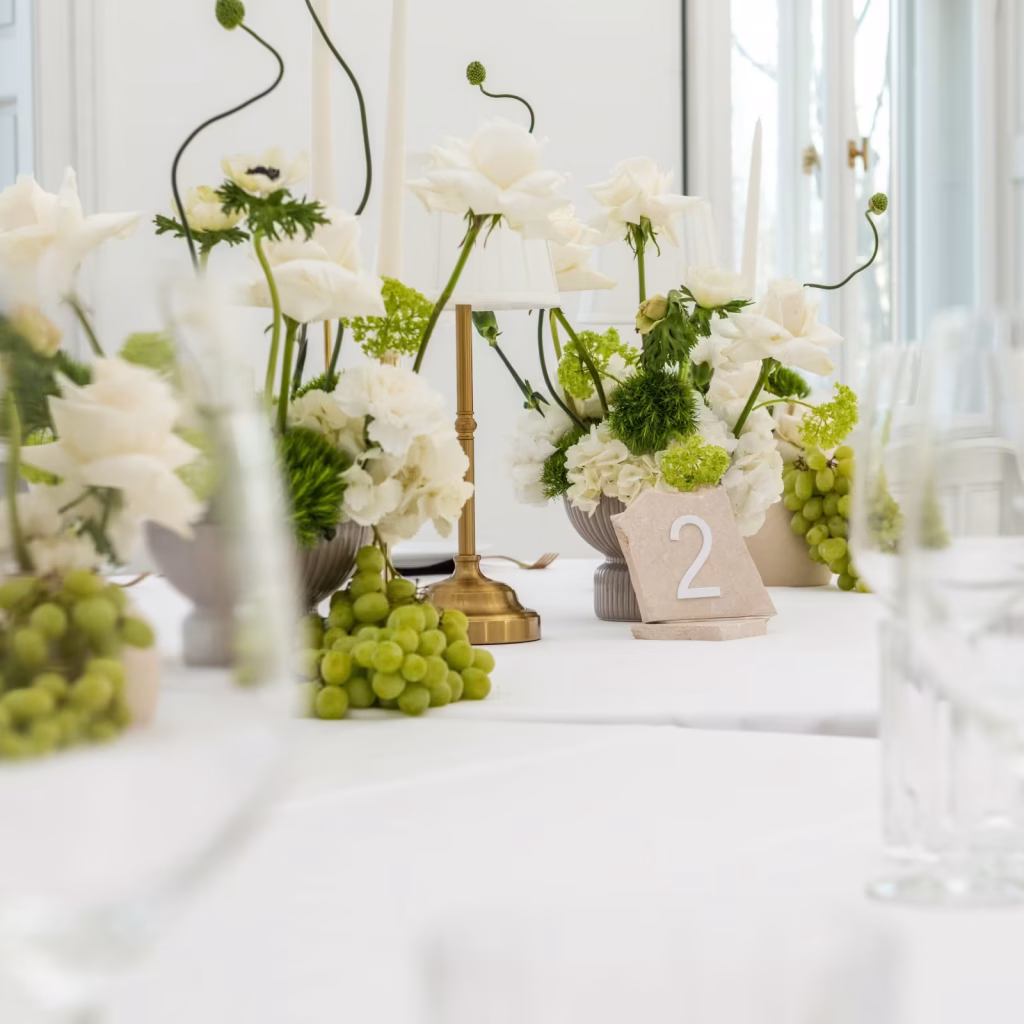 Weiße Blumenarrangements mit Trauben und Kerzen schmücken die festliche Hochzeitstafel. Hochzeitsfloristik - blumenkultur